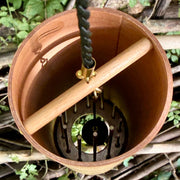the inside of A natural Koshi River Earth Symphony Cherry wind chime hanging outdoors from a tree trunk, with a small wooden tag below and a black hanging cord, set against a forest background.