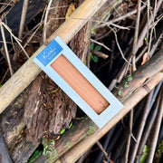 A natural Koshi River Earth Symphony  cherry wood wind chime hanging outdoors from a tree trunk, with a small wooden tag below and a black hanging cord, set against a forest background.