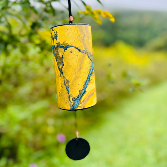 golden colored Zaphir chime hanging from a blooming tree branch over a meadow  |Weplaywelltogether.