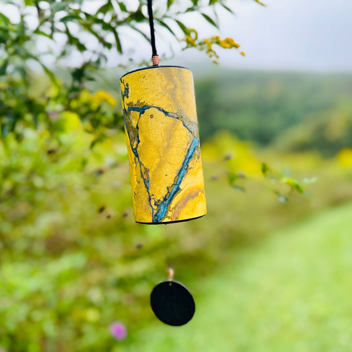 golden colored Zaphir chime hanging from a blooming tree branch over a green valley meadow  |Weplaywelltogether.
