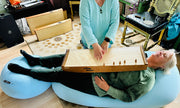 a woman laying on a moon pod while with feeltone monochord on top of her body and another woman playing it | weplaywelltogether