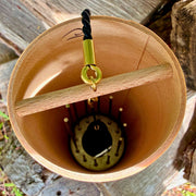 The inside of A natural Koshi Ocean  Earth Symphony maple wind chime hanging outdoors from a tree trunk, with a small wooden tag below and a black hanging cord, set against a forest background.