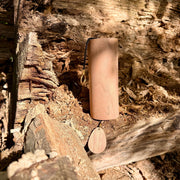 A natural Koshi Mountain Earth Symphony Walnut wind chime hanging outdoors from a tree trunk, with a small wooden tag below and a black hanging cord, set against a forest background.