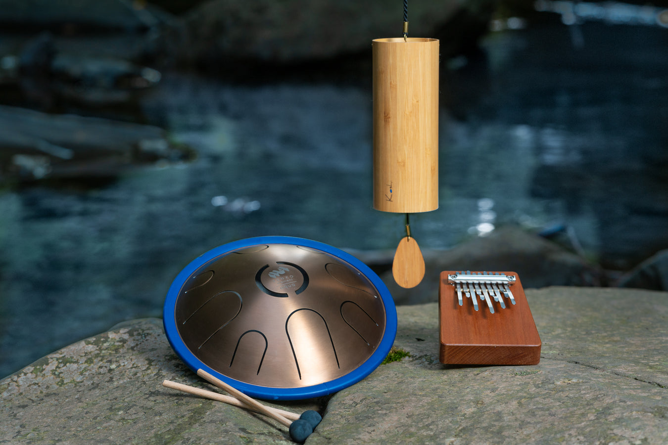 Set of instruments on a rock by the river. Aqua metal tongue drum by Metal Sound, Hokema Aqua B9 kalimba and Aqua chime by Koshi all tuned into water element. | weplaywelltogether