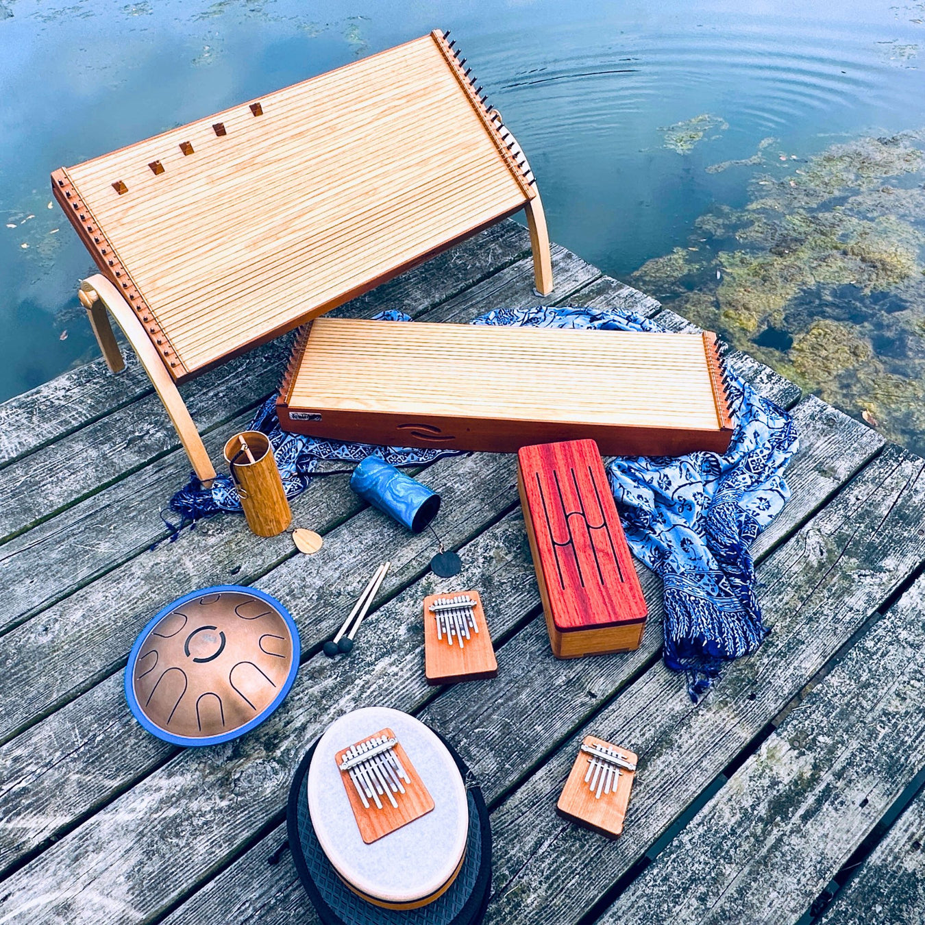 feeltone 34 string Monolina and 21 string Monolini, Zenko elemental aqua tongue drum, Hokema Sansula basic, B9 and B5 kalimbas in aqua tuning, feeltone aqua tinka tong, Koshi chiem aqua and blue Zaphir chime on a pier by the water | weplaywelltogether